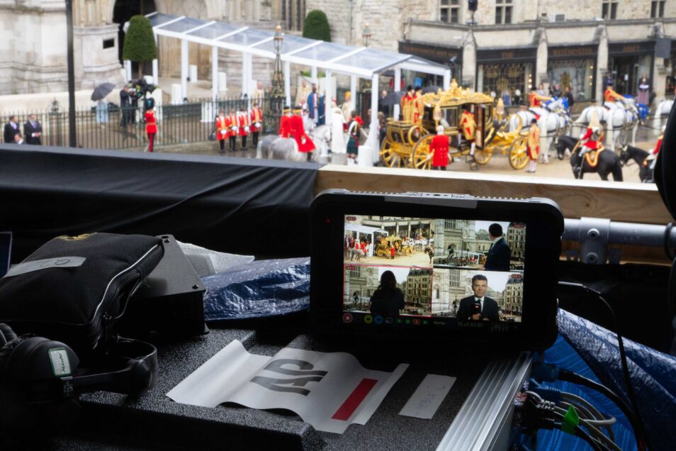 Video monitor showing images of live news reporters in front of horse drawn gold coach at westminster abbey during srt video streaming at coronation of king charles iii