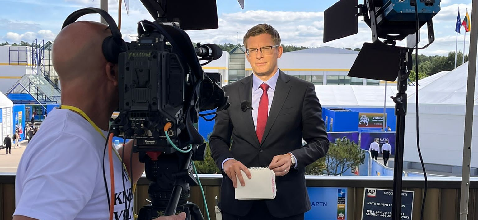 Man wearing suit and tie looking at a video camera for live news reporting