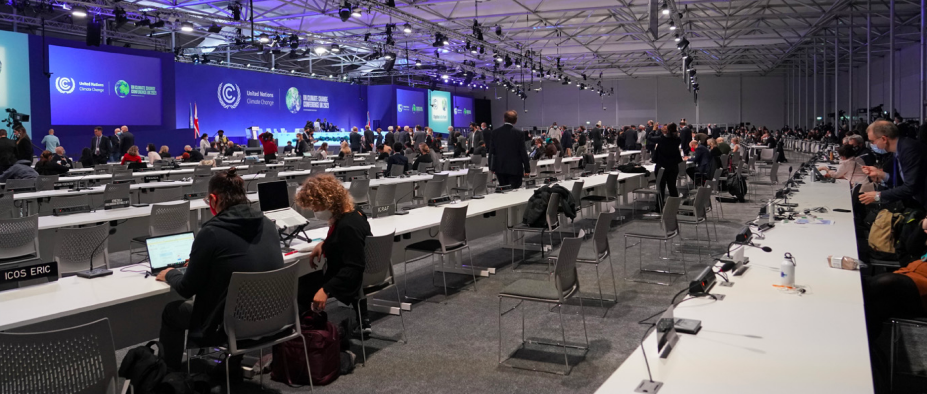 People sitting at desks in front of podium with blue screen at un climate talks in Glasgow 2021