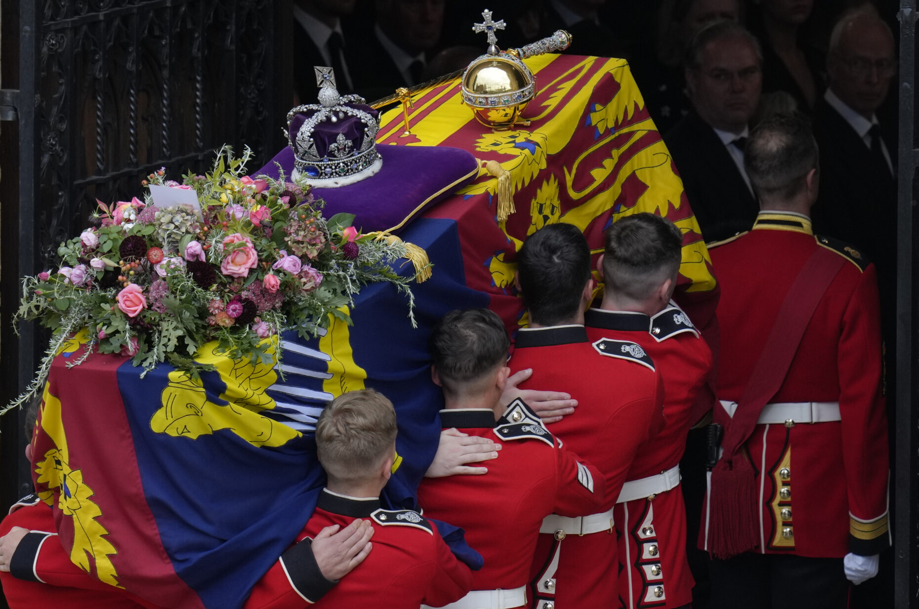 Military personnel in red ceremonial uniforms carrying a coffin adorned with flowers and a crown at the state funeral of queen elizabeth ii